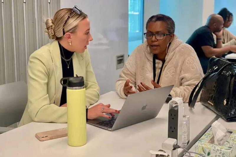 two people discussing something while sitting on a desk