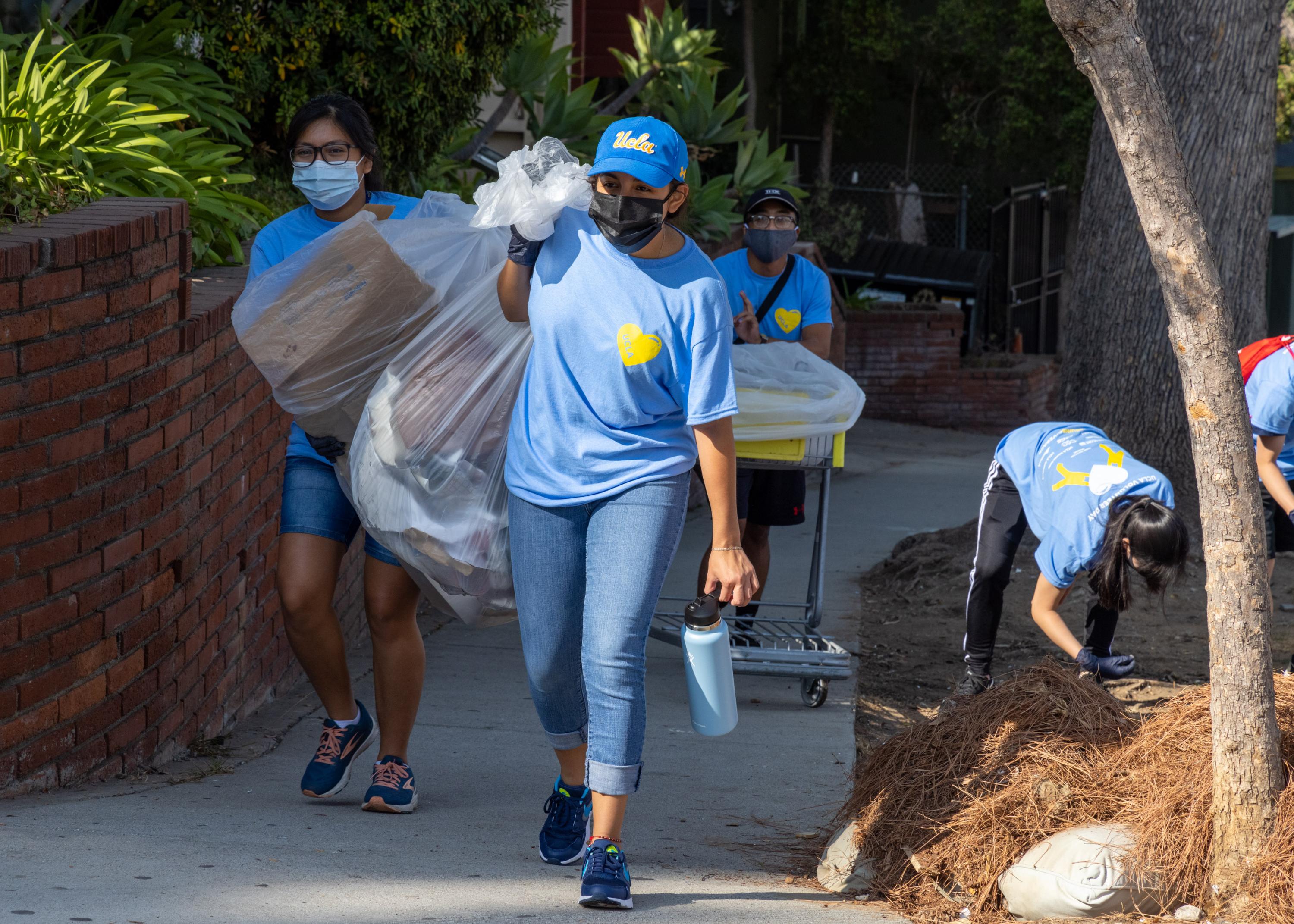 Photo of volunteers carrying trash bags from a street cleanup event. They are masked and wearing light blue UCLA Volunteer Day t-shirts.