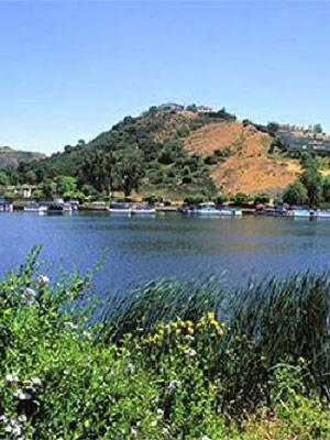 The photo shows a landscape in Conejo Valley. There is a hill, with a body of water below, and some plants and other greenery at the bottom of the photo.