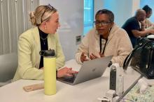 two people discussing something while sitting on a desk