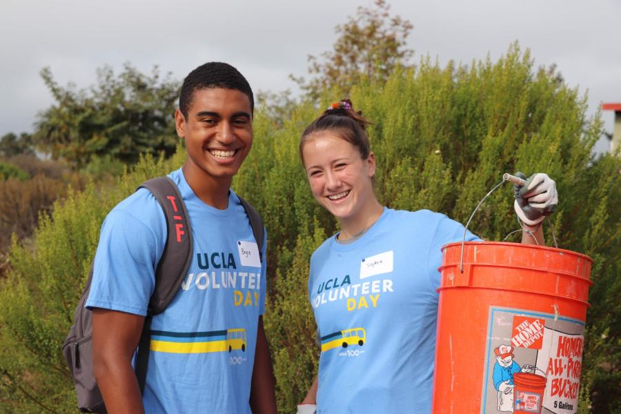 two students holding a bucket in a field
