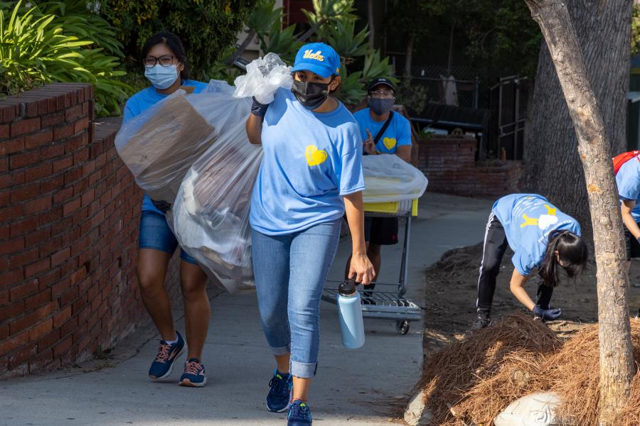 Photo of volunteers carrying trash bags from a street cleanup event. They are masked and wearing light blue UCLA Volunteer Day t-shirts.